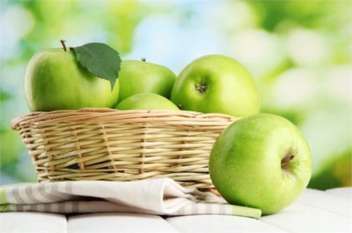 成熟的绿苹果，篮子里的叶子，木桌上，绿色的背上。